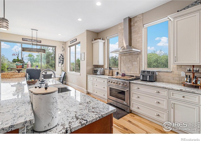 kitchen featuring light wood-style flooring, wall chimney range hood, high end range, light stone countertops, and pendant lighting