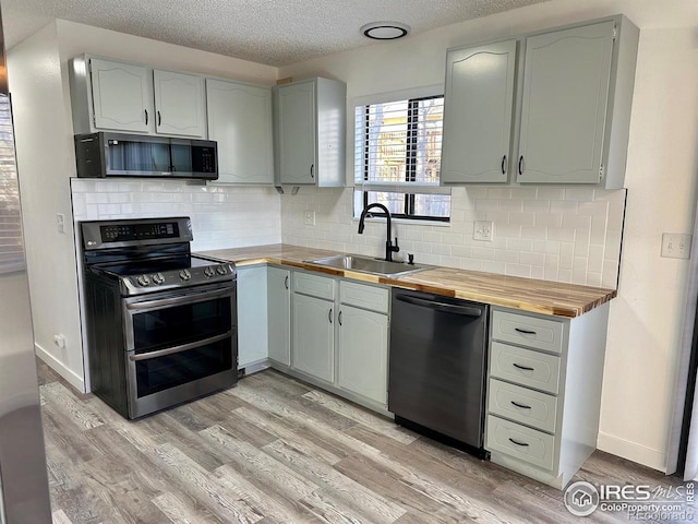 kitchen with a sink, wood counters, double oven range, dishwasher, and light wood finished floors