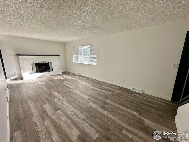 unfurnished living room featuring a fireplace, baseboards, dark wood finished floors, and a textured ceiling