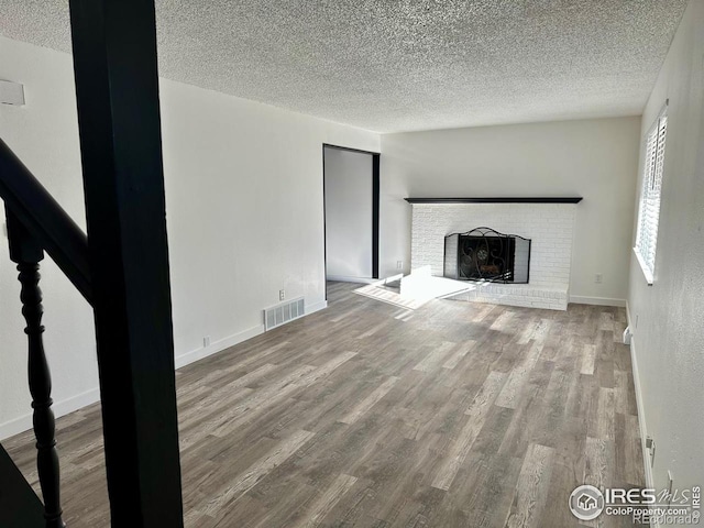 unfurnished living room featuring visible vents, a brick fireplace, a textured ceiling, wood finished floors, and baseboards