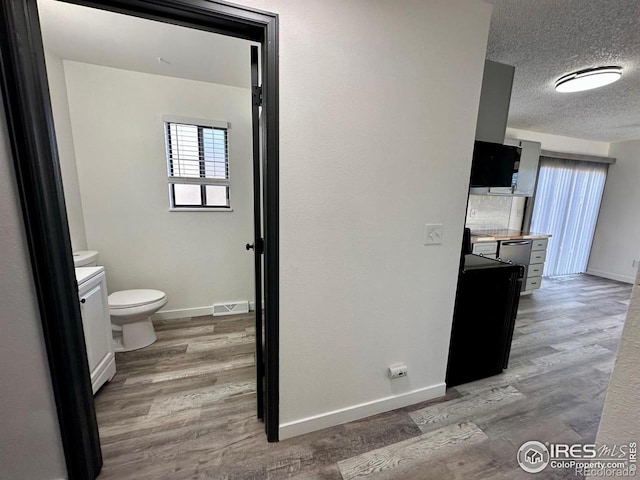 interior space with a textured ceiling, toilet, wood finished floors, visible vents, and baseboards