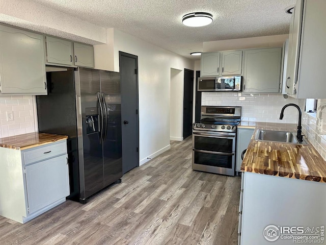 kitchen featuring light wood finished floors, butcher block counters, appliances with stainless steel finishes, and a sink