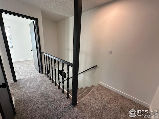 stairs featuring carpet, baseboards, and a textured ceiling