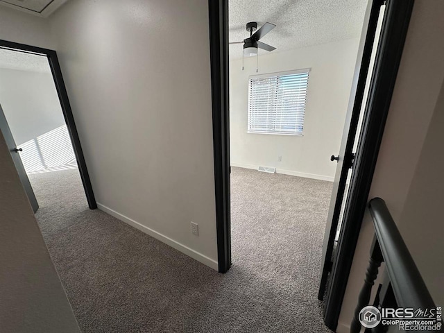 corridor with a textured ceiling, carpet floors, visible vents, and baseboards