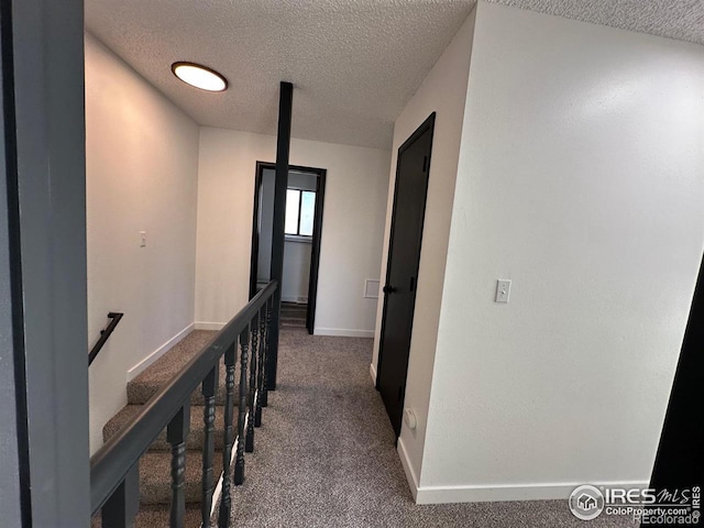 hallway featuring dark colored carpet, baseboards, a textured ceiling, and an upstairs landing