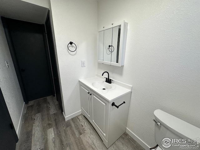 half bath with a textured wall, toilet, vanity, wood finished floors, and baseboards