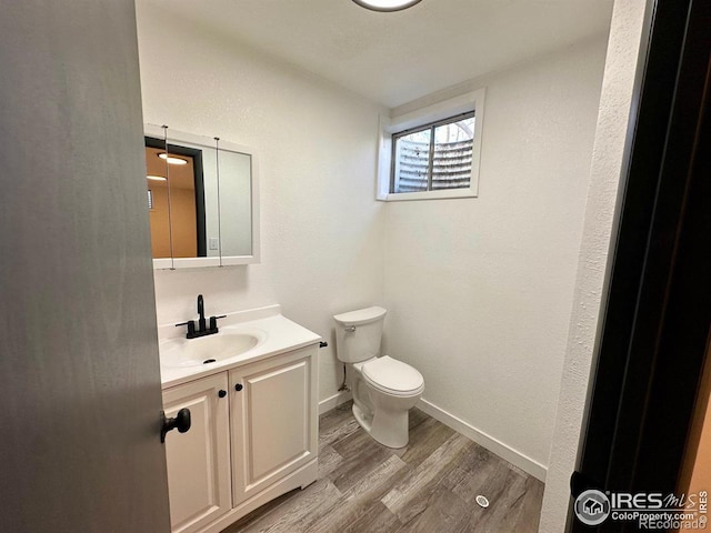 half bathroom with toilet, baseboards, wood finished floors, and vanity