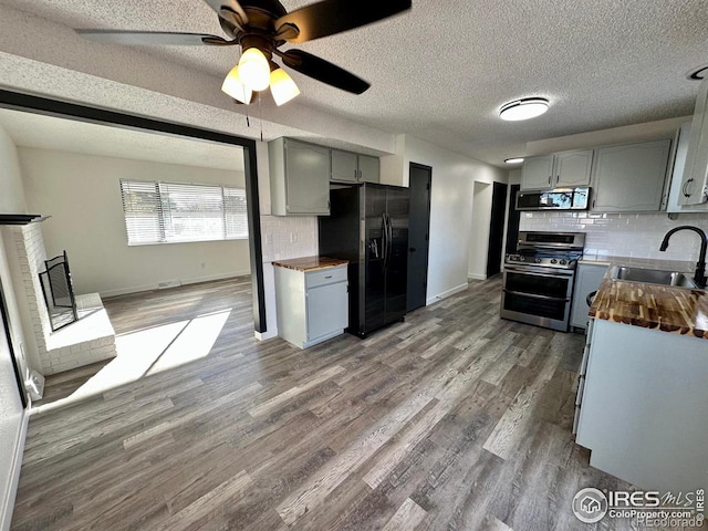 kitchen with gray cabinetry, wood finished floors, a sink, wooden counters, and appliances with stainless steel finishes