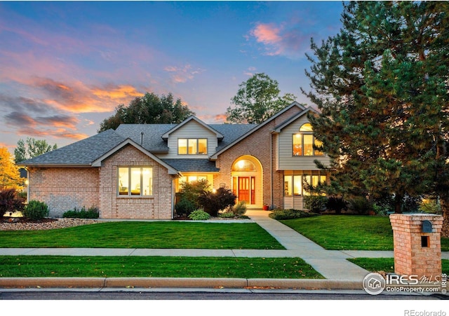 traditional home featuring a shingled roof, a front lawn, and brick siding