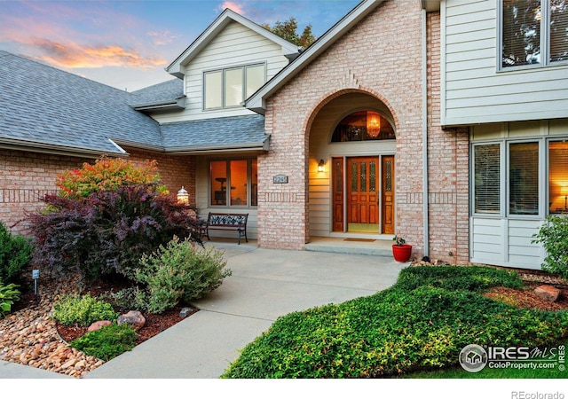 exterior entry at dusk with brick siding and a shingled roof