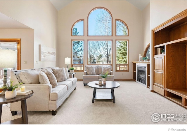 living room with carpet floors, a glass covered fireplace, and high vaulted ceiling