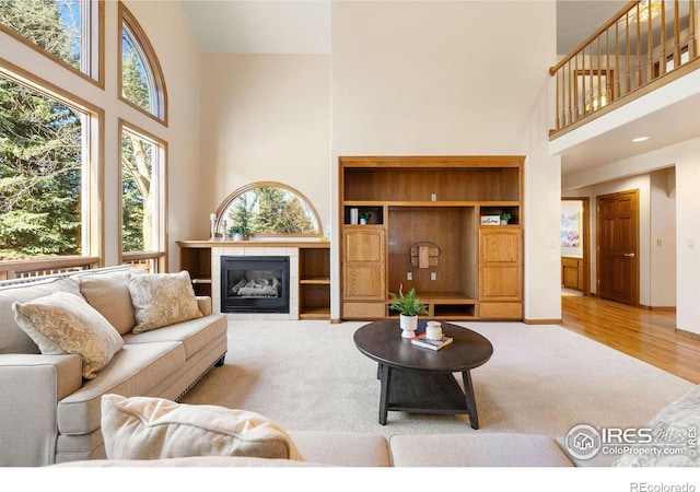 living area with wood finished floors, carpet flooring, a tile fireplace, and a towering ceiling