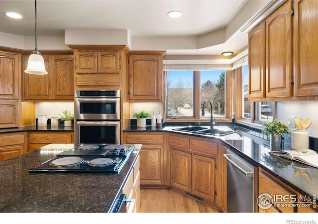 kitchen featuring a sink, appliances with stainless steel finishes, brown cabinetry, dark stone countertops, and pendant lighting