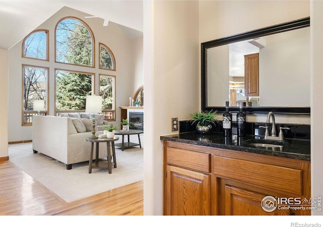 bar with high vaulted ceiling, a glass covered fireplace, a sink, and light wood-style floors