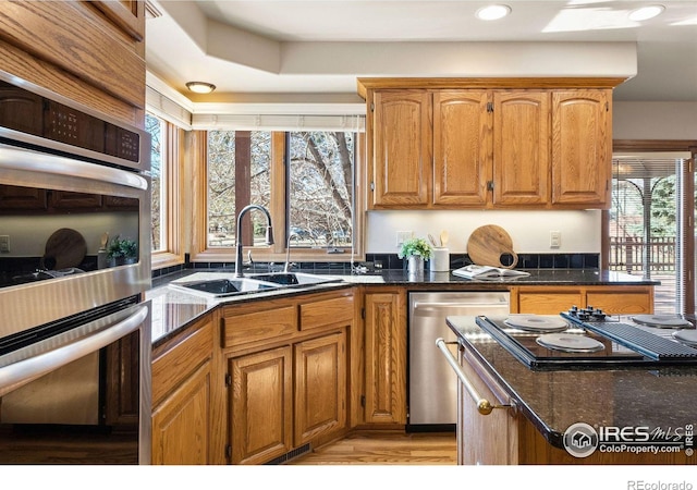 kitchen featuring appliances with stainless steel finishes, dark stone countertops, a sink, and brown cabinets