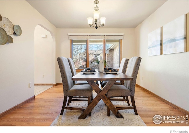 dining space with light wood-type flooring, arched walkways, baseboards, and an inviting chandelier