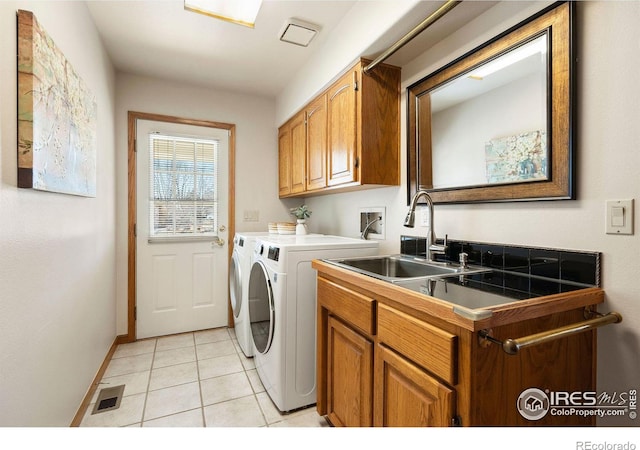 clothes washing area featuring washing machine and clothes dryer, cabinet space, visible vents, light tile patterned flooring, and a sink