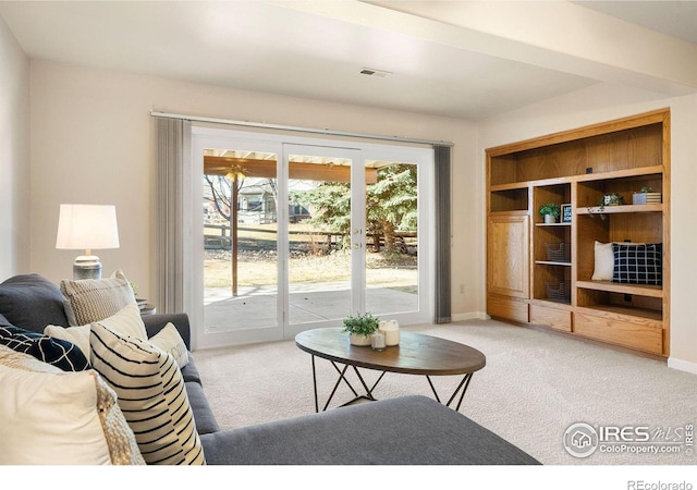 living area featuring baseboards, visible vents, and light colored carpet