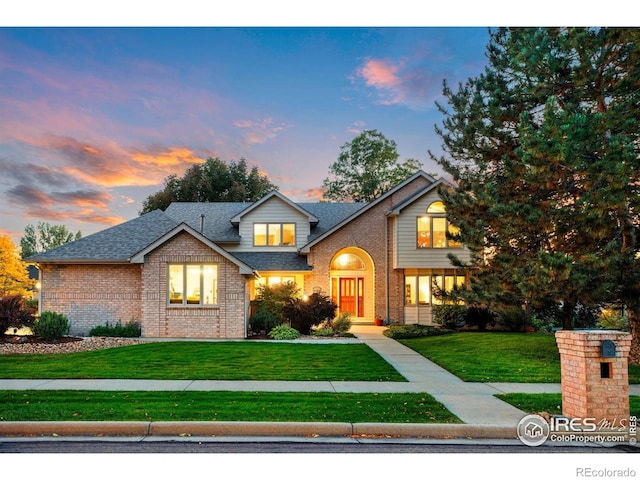 traditional-style home with a shingled roof, a front yard, and brick siding
