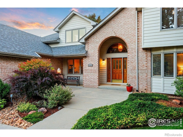 exterior entry at dusk with brick siding and roof with shingles