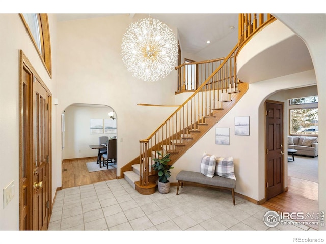 entrance foyer featuring arched walkways, a towering ceiling, a notable chandelier, and stairway