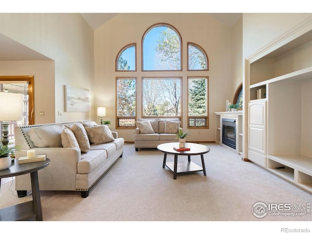 living area with light colored carpet, a glass covered fireplace, and a high ceiling