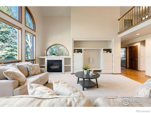 living area with a tiled fireplace, a towering ceiling, wood finished floors, and built in shelves