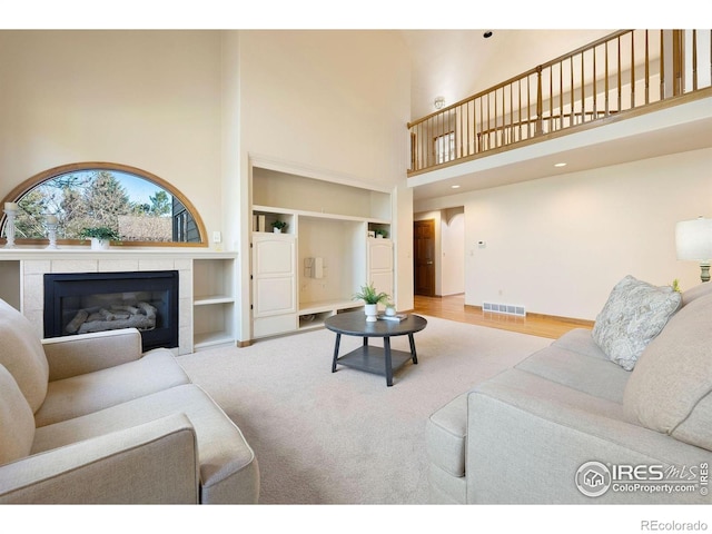 living room featuring visible vents, built in features, baseboards, a high ceiling, and a tile fireplace