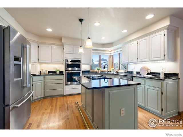 kitchen with decorative light fixtures, dark countertops, white cabinets, light wood-style floors, and stainless steel appliances