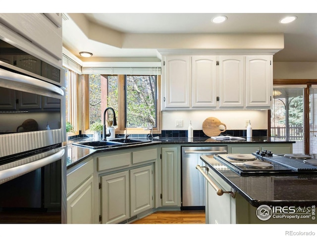 kitchen with light wood finished floors, white cabinets, a sink, dark stone countertops, and appliances with stainless steel finishes