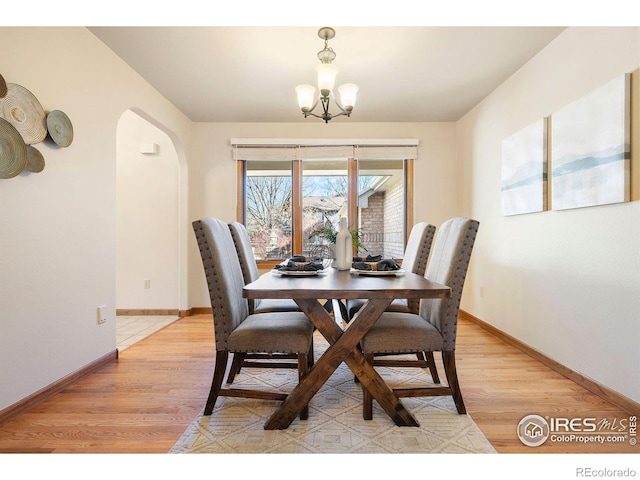 dining space with light wood-style floors, arched walkways, baseboards, and a notable chandelier