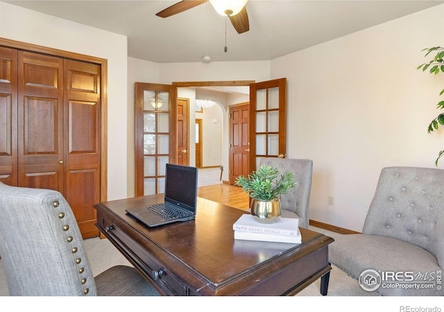 office area featuring light colored carpet, arched walkways, baseboards, and ceiling fan