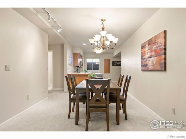 dining area with an inviting chandelier, baseboards, rail lighting, and light colored carpet