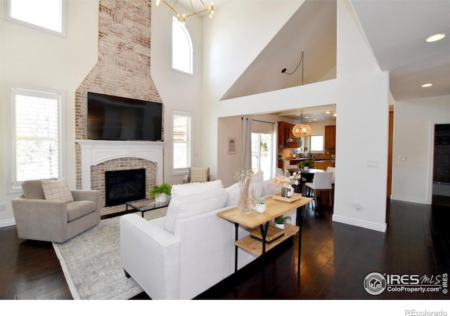 living room featuring dark wood-type flooring, a brick fireplace, a notable chandelier, and baseboards