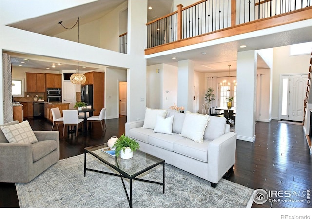 living area with an inviting chandelier, a high ceiling, baseboards, and dark wood-style flooring