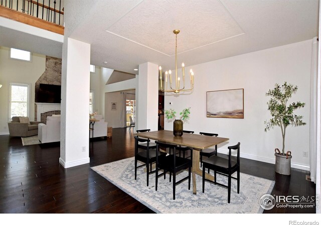 dining space with baseboards, dark wood-style flooring, a fireplace, and a notable chandelier