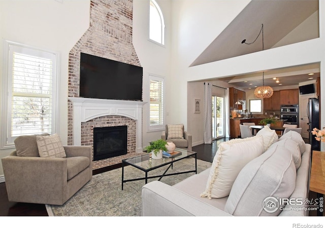 living area featuring a brick fireplace, a high ceiling, baseboards, and wood finished floors