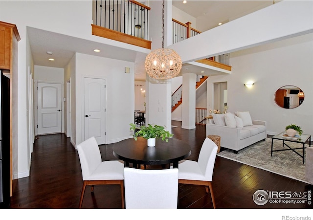 dining space with a chandelier, a towering ceiling, baseboards, stairway, and dark wood finished floors