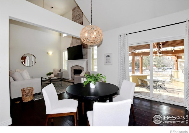 dining space featuring a towering ceiling, a brick fireplace, and dark wood-type flooring