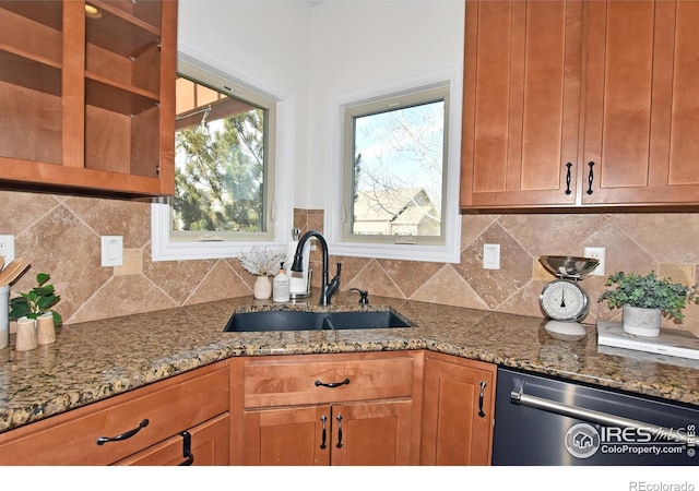 kitchen featuring light stone counters, a sink, stainless steel dishwasher, backsplash, and brown cabinets