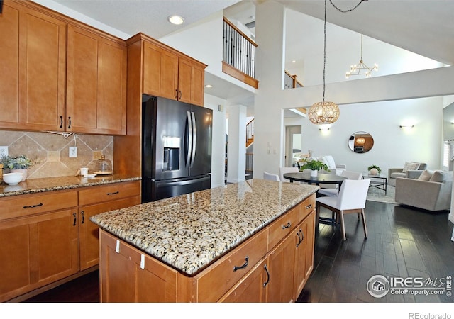 kitchen featuring hanging light fixtures, black refrigerator with ice dispenser, brown cabinetry, dark wood finished floors, and an inviting chandelier