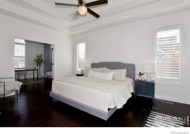 bedroom featuring dark wood-type flooring, a raised ceiling, and baseboards