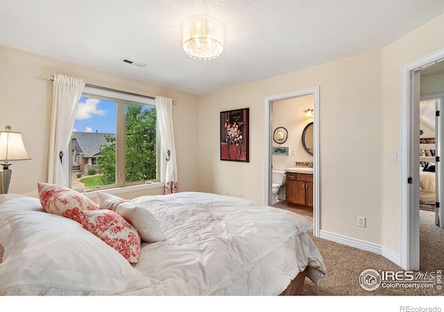 bedroom with ensuite bathroom, a textured ceiling, carpet floors, visible vents, and baseboards