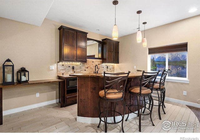 kitchen with tasteful backsplash, hanging light fixtures, light wood-style floors, a sink, and dark brown cabinets