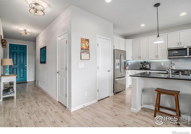 kitchen with white cabinets, appliances with stainless steel finishes, tasteful backsplash, dark countertops, and pendant lighting