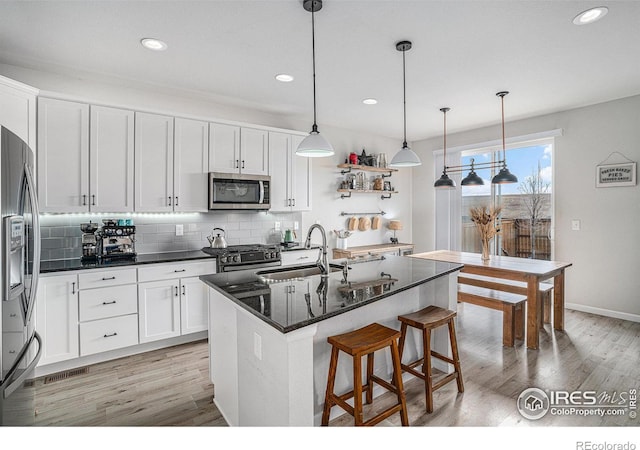 kitchen featuring appliances with stainless steel finishes, white cabinets, a center island with sink, and hanging light fixtures