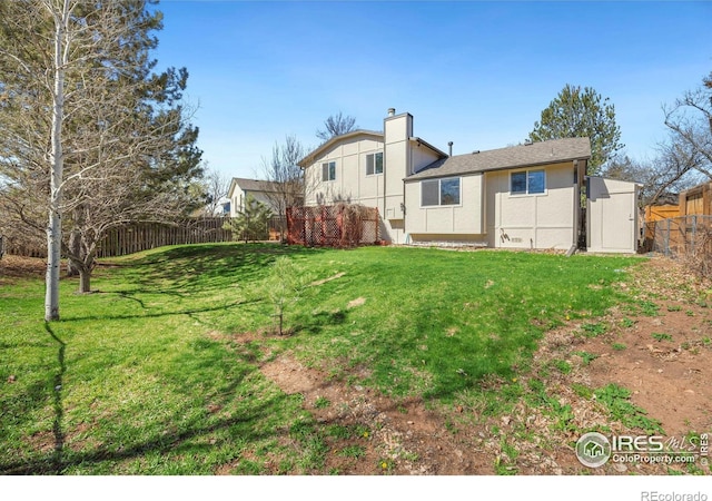 rear view of property with a chimney, fence, a lawn, and stucco siding