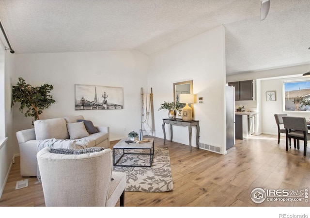 living room featuring lofted ceiling, visible vents, a textured ceiling, and light wood finished floors