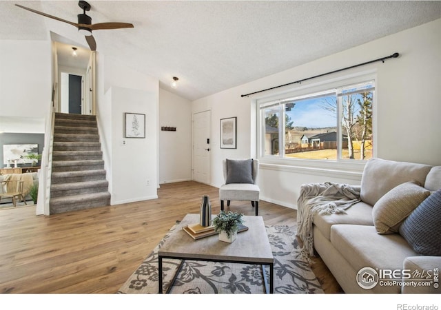 living area with stairway, vaulted ceiling, a textured ceiling, light wood-type flooring, and baseboards