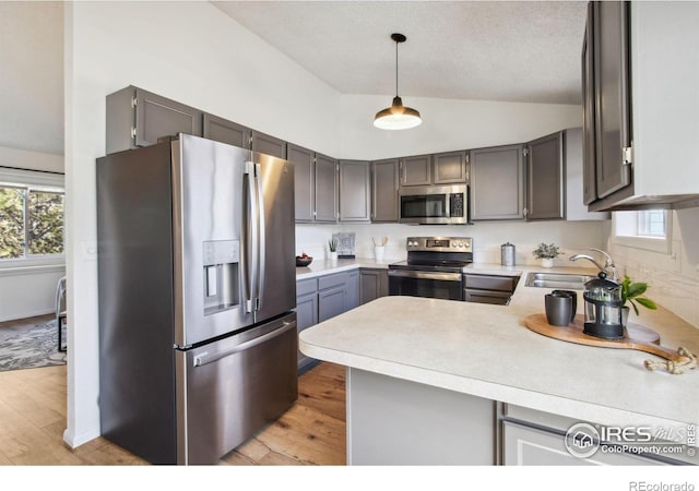 kitchen featuring light countertops, hanging light fixtures, appliances with stainless steel finishes, a sink, and a peninsula